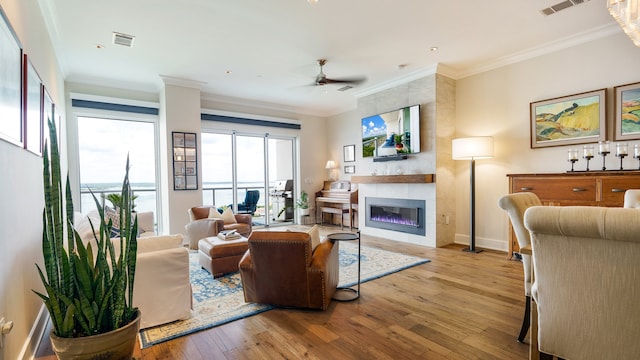 living room featuring ceiling fan, crown molding, light hardwood / wood-style flooring, and a large fireplace