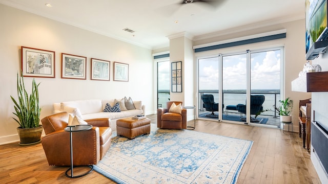 living room featuring a water view, ceiling fan, light hardwood / wood-style floors, a fireplace, and ornamental molding