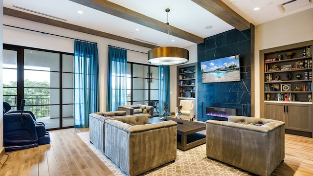 living room featuring built in shelves, beam ceiling, a fireplace, and light wood-type flooring