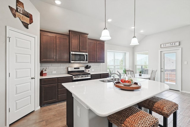 kitchen with backsplash, a kitchen island with sink, hanging light fixtures, appliances with stainless steel finishes, and vaulted ceiling