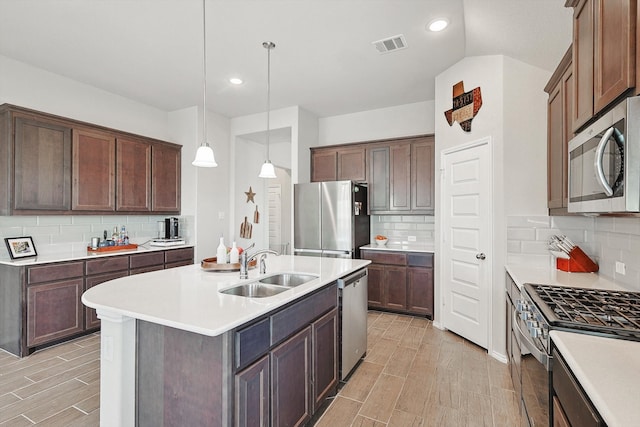 kitchen featuring tasteful backsplash, stainless steel appliances, pendant lighting, sink, and a center island with sink