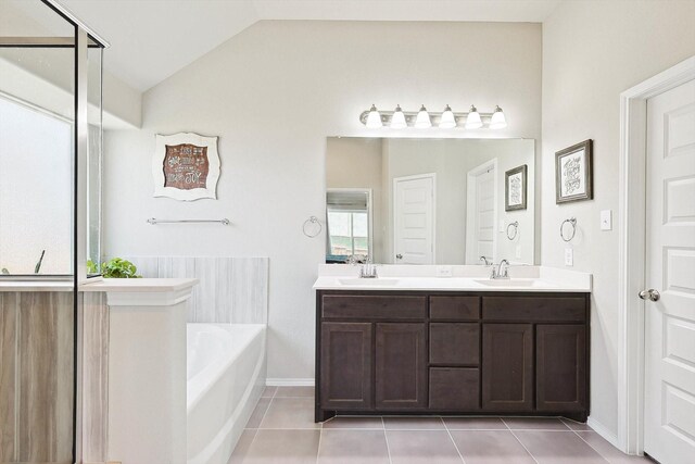 bathroom with vaulted ceiling, tile patterned flooring, a bathing tub, and dual bowl vanity