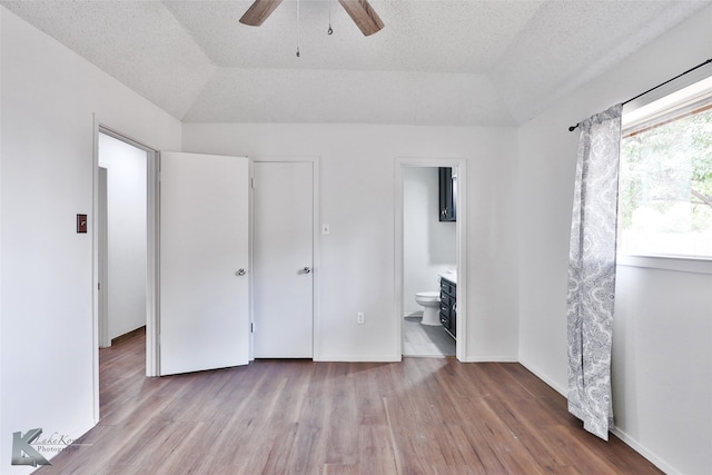 unfurnished bedroom with hardwood / wood-style flooring, a raised ceiling, ensuite bathroom, and ceiling fan