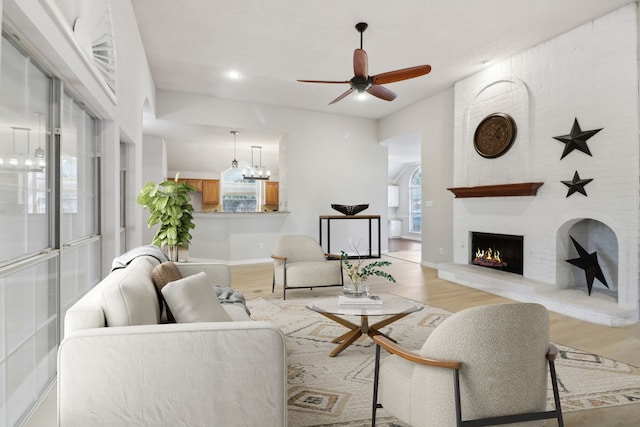 living room with brick wall, a fireplace, light wood-type flooring, and ceiling fan