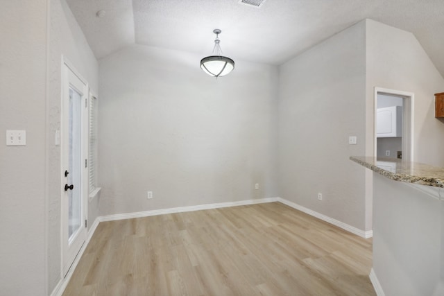 unfurnished dining area with lofted ceiling, light wood-type flooring, and a textured ceiling