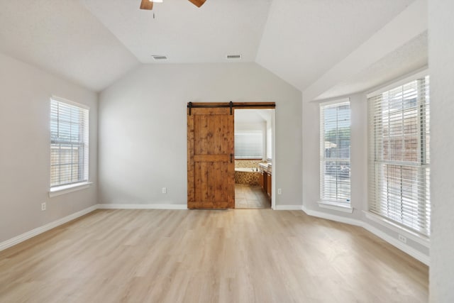 unfurnished living room with light hardwood / wood-style floors, vaulted ceiling, a barn door, and ceiling fan