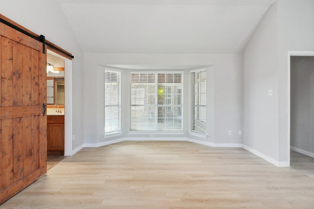 empty room with vaulted ceiling, sink, light wood-type flooring, and a barn door