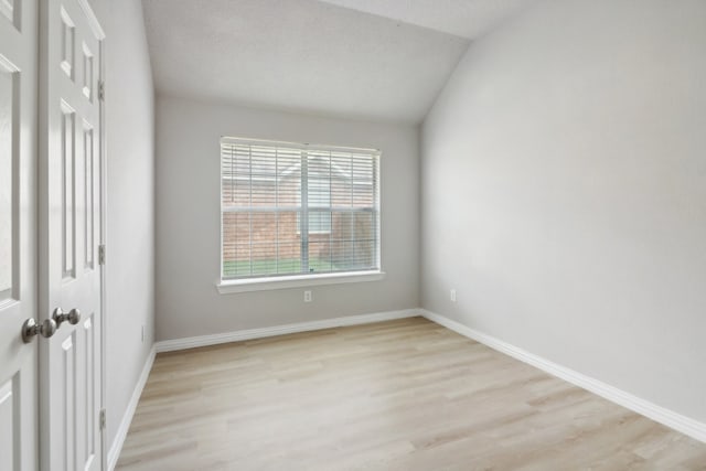 unfurnished room with a textured ceiling, lofted ceiling, and light wood-type flooring