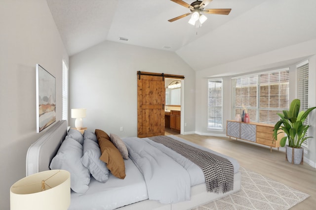 bedroom with connected bathroom, light hardwood / wood-style floors, a barn door, lofted ceiling, and ceiling fan