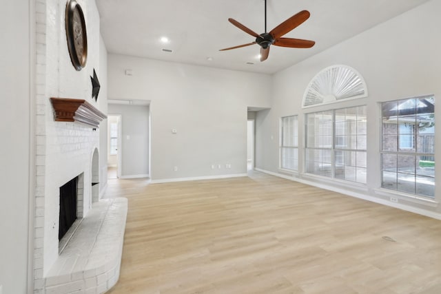 unfurnished living room featuring a fireplace, high vaulted ceiling, light wood-type flooring, and ceiling fan