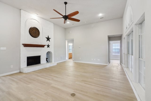 unfurnished living room with light wood-type flooring, a high ceiling, ceiling fan, brick wall, and a fireplace