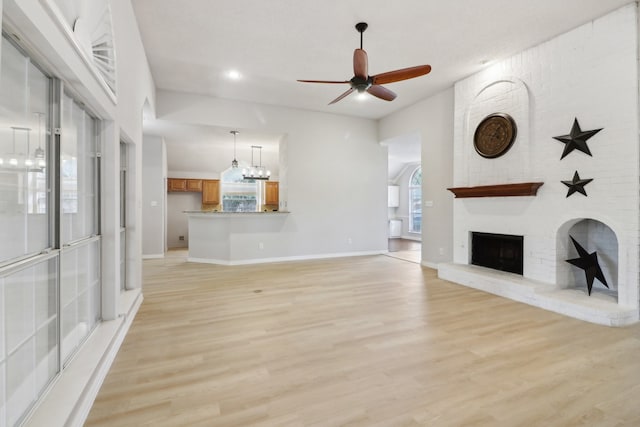 unfurnished living room featuring a fireplace, light hardwood / wood-style floors, brick wall, and ceiling fan