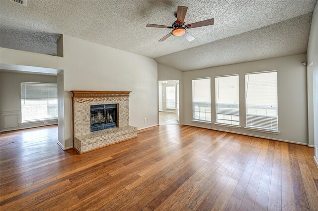 unfurnished living room with hardwood / wood-style flooring, a fireplace, a textured ceiling, lofted ceiling, and ceiling fan