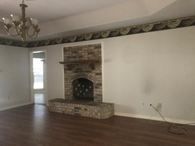 unfurnished living room featuring a brick fireplace, a notable chandelier, and dark hardwood / wood-style flooring