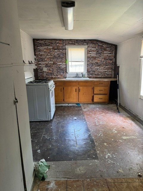 kitchen featuring white range with gas cooktop, sink, dark tile patterned floors, and lofted ceiling