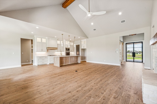 unfurnished living room featuring beam ceiling, light wood-type flooring, ceiling fan, and high vaulted ceiling