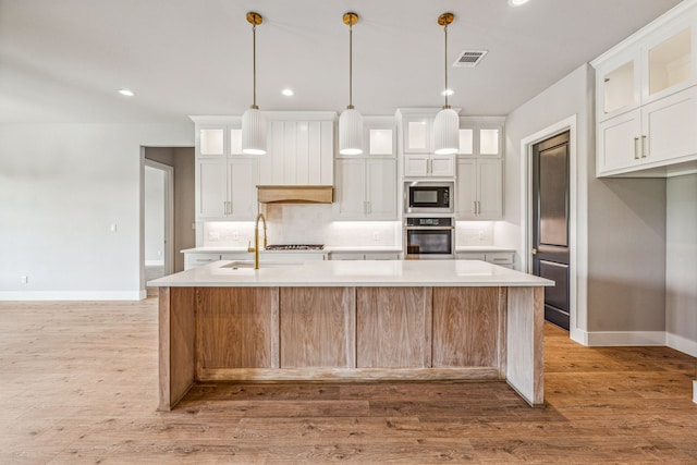 kitchen featuring oven, an island with sink, white cabinets, and light wood-type flooring