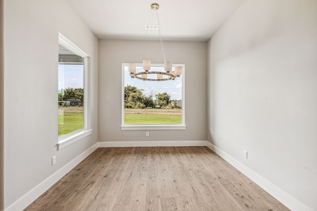 unfurnished dining area with a notable chandelier and light wood-type flooring