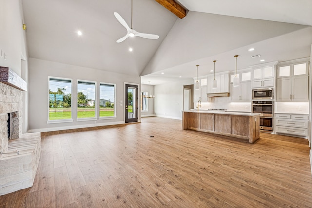 kitchen with white cabinets, a fireplace, light hardwood / wood-style floors, decorative light fixtures, and high vaulted ceiling