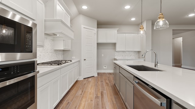 kitchen with appliances with stainless steel finishes, tasteful backsplash, sink, pendant lighting, and white cabinetry