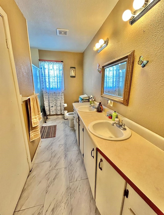 bathroom with dual vanity, toilet, tile patterned floors, and a textured ceiling