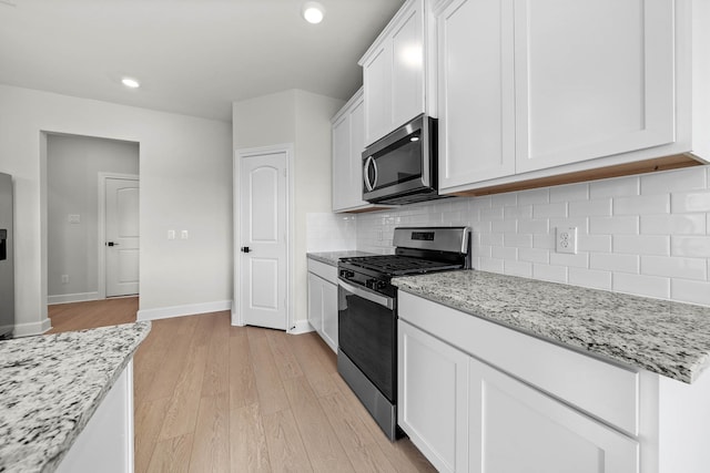 kitchen with white cabinetry, light wood-type flooring, backsplash, light stone counters, and stainless steel appliances