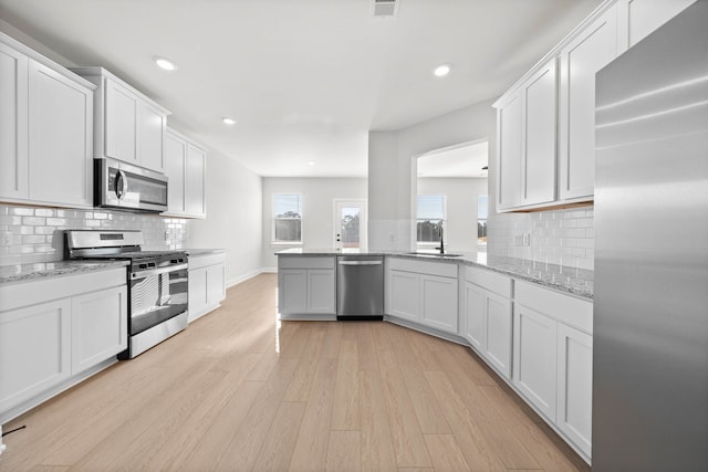 kitchen with decorative backsplash, white cabinetry, appliances with stainless steel finishes, and light wood-type flooring