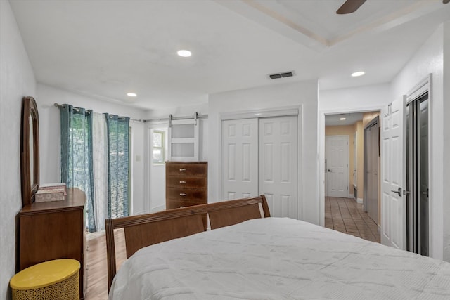 bedroom featuring a barn door, tile patterned floors, ceiling fan, and a closet