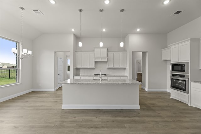 kitchen with light stone countertops, stainless steel oven, white cabinets, and an island with sink