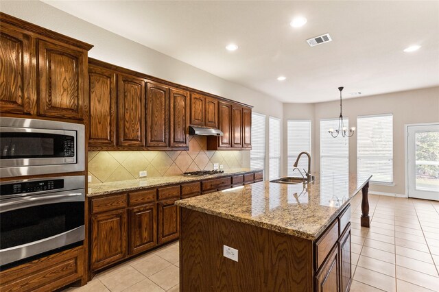 kitchen with light stone countertops, stainless steel appliances, a chandelier, sink, and a kitchen island with sink