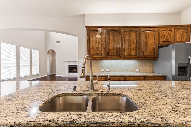 kitchen with light stone countertops, stainless steel refrigerator with ice dispenser, hardwood / wood-style floors, sink, and decorative backsplash