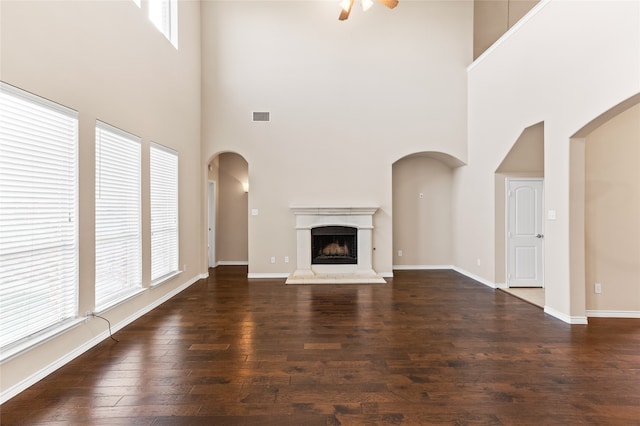 unfurnished living room with dark wood-type flooring, ceiling fan, and a high ceiling