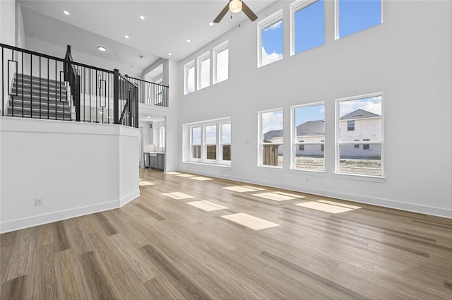 unfurnished living room with ceiling fan, light hardwood / wood-style floors, and a high ceiling