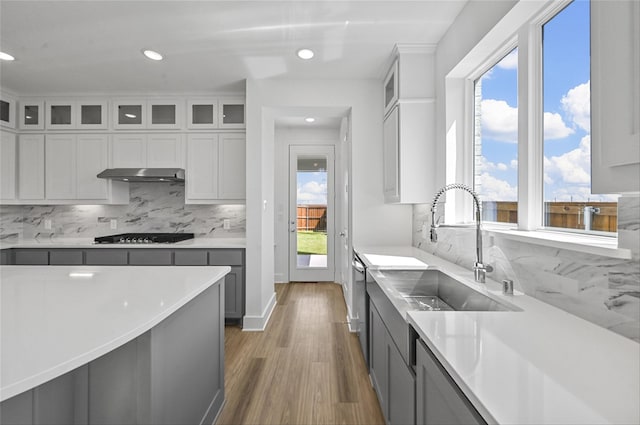 kitchen featuring dark wood-type flooring, sink, black gas stovetop, gray cabinetry, and backsplash