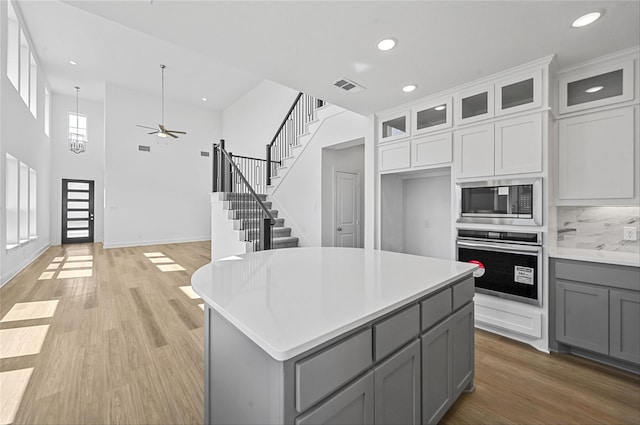 kitchen featuring appliances with stainless steel finishes, backsplash, gray cabinets, a center island, and ceiling fan