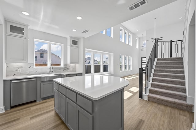 kitchen featuring tasteful backsplash, gray cabinetry, a kitchen island, dishwasher, and light wood-type flooring