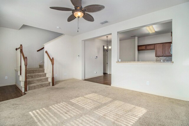 unfurnished living room featuring ceiling fan with notable chandelier and dark colored carpet