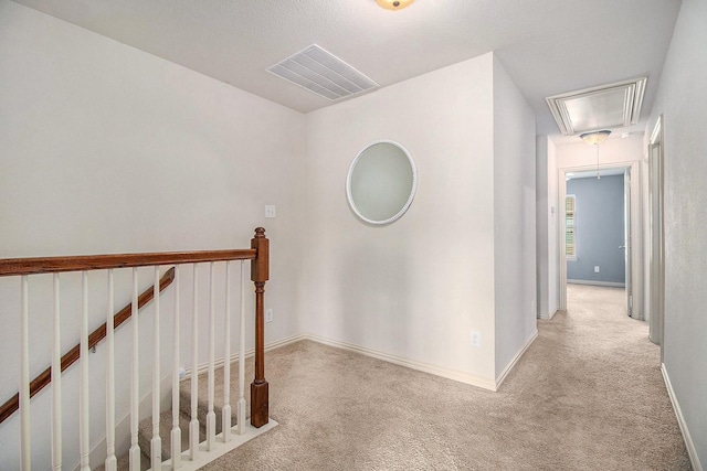 corridor with visible vents, attic access, light carpet, an upstairs landing, and baseboards