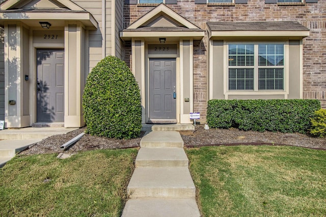 view of exterior entry featuring brick siding and a lawn