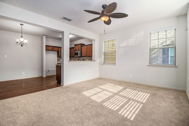 unfurnished living room with baseboards, visible vents, dark carpet, and ceiling fan with notable chandelier