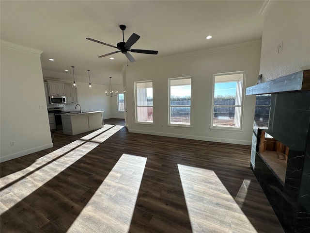 living room featuring a tile fireplace, dark hardwood / wood-style floors, ceiling fan with notable chandelier, sink, and ornamental molding