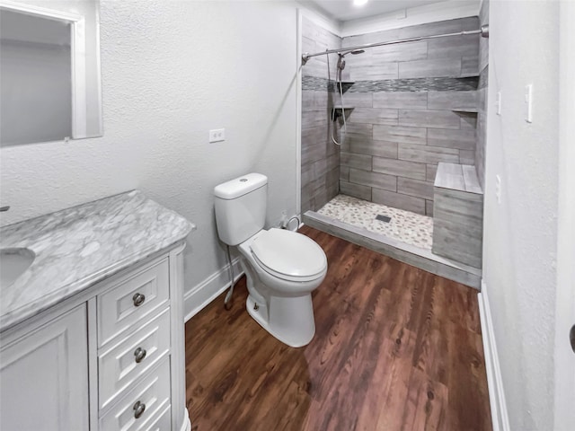 bathroom with hardwood / wood-style floors, vanity, tiled shower, and toilet