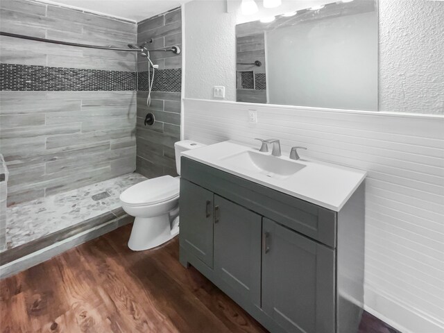 bathroom with a tile shower, vanity, hardwood / wood-style floors, and toilet