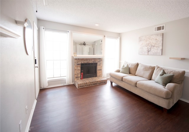 living room with ceiling fan, dark hardwood / wood-style flooring, a brick fireplace, and a textured ceiling