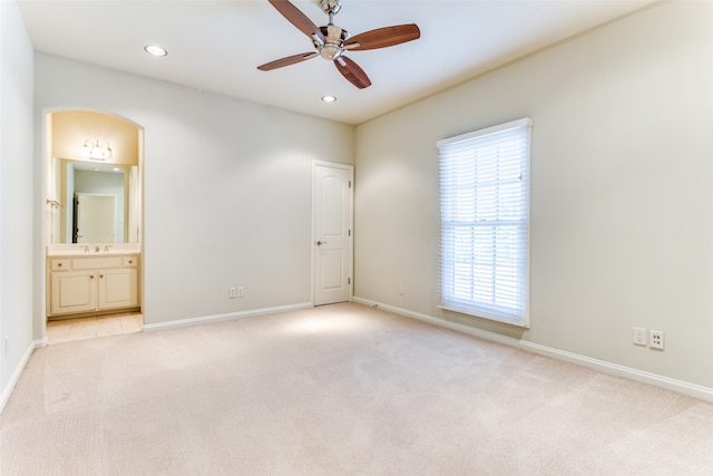 unfurnished bedroom featuring light colored carpet, ensuite bathroom, and ceiling fan