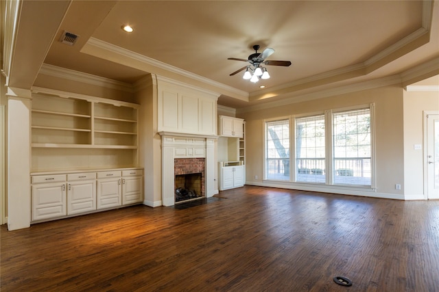 unfurnished living room featuring dark hardwood / wood-style flooring, a tray ceiling, ornamental molding, a brick fireplace, and ceiling fan