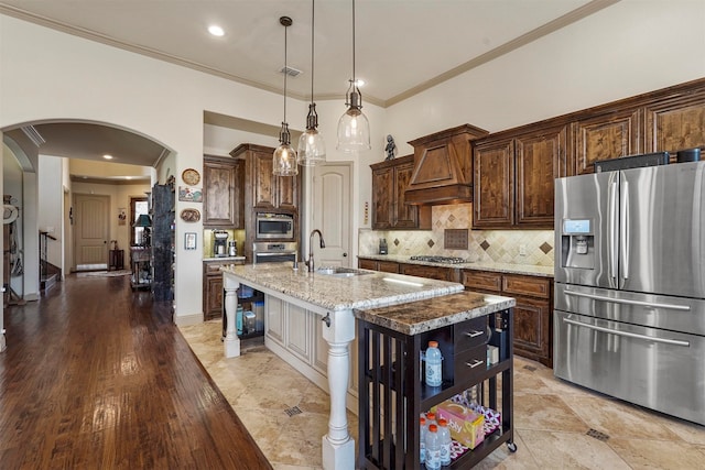 kitchen with light hardwood / wood-style flooring, premium range hood, an island with sink, appliances with stainless steel finishes, and sink