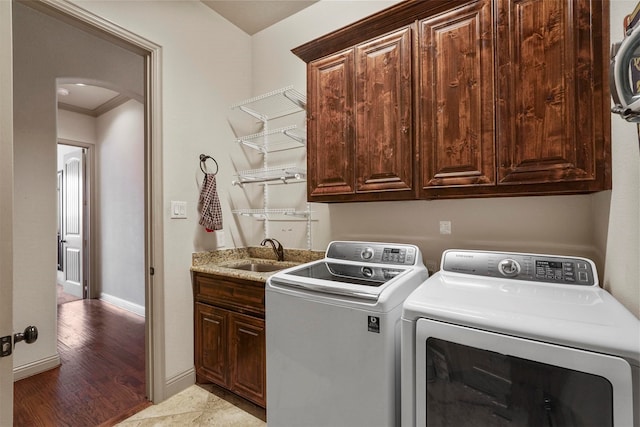 clothes washing area with crown molding, light hardwood / wood-style flooring, washing machine and dryer, cabinets, and sink