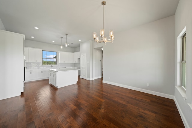 kitchen with white cabinets, hanging light fixtures, backsplash, a kitchen island, and dark hardwood / wood-style floors