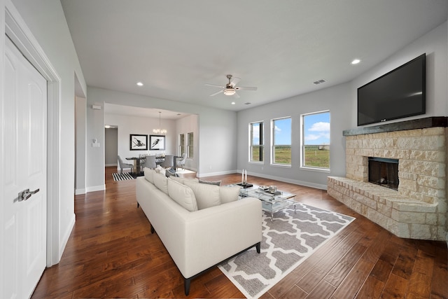 living room with a fireplace, dark wood-type flooring, and ceiling fan with notable chandelier